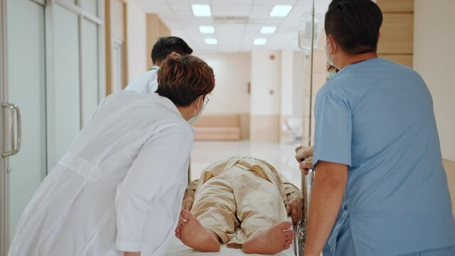 Group of Asian emergency doctor and nurse team wear face mask, push emergency stretcher, transport senior patient in hospital. Health care paramedic service, or medical rescue team operation concept