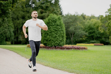 athletic man with dark hair running on a treadmill in a white t-shirt, doing sports in a green...