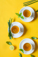 Herbal green tea with lemongrass in glass cup with fresh limes. Top view of three white cups of Lemon Grass Drink on a Yellow Background.