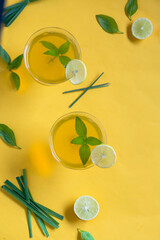 Herbal green tea with lemongrass in glass cup with fresh limes. Top view of two cups of Lemon Grass Drink on a Yellow Background.