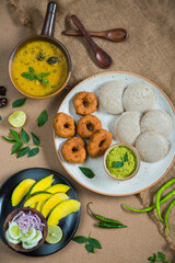 Top view of Idli, Wada, Sambar and Chutney. Traditional South Indian food, surrounded with lemon, raw mango and green chillies.