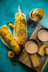 Top view of brewed hot milk tea with roasted grilled corn and fresh toast. Delicious Grilled Corncobs and Two Cups of Masala Chai, an ideal Indian monsoon brunch good for boosting immunity and health.