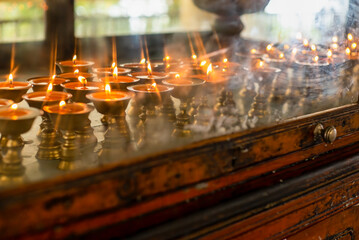 Dharamsala Temple candles in brass holders glow through worn glass cabinet door