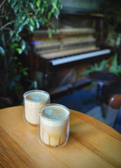 two cups of latte with milk froth in the form of a heart on the background of which a piano in green plants
