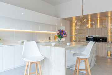 luxury interior design of modern trendy snow white kitchen in minimalistic style with island and two bar stools. huge windows to the floor and a glass rack for dishes