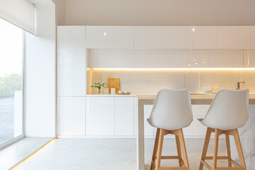 luxury interior design of modern trendy snow white kitchen in minimalistic style with island and two bar stools. huge windows to the floor and a glass rack for dishes