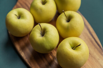 yellow golden delicious apples on green table, wooden cutting board 