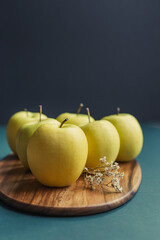 yellow golden delicious apples on green table, wooden cutting board and black background