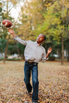 A young African American boy playing catch with a football in a park