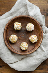 Fototapeta na wymiar Homemade raw vegan sweets energy balls in coconut shavings in ceramic plate on old wooden table