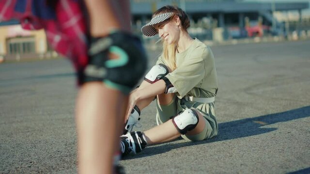 Smiling woman sitting on ground and putting roller skates waving his hand feel happy street in summertime legs rollerblading activity slow motion