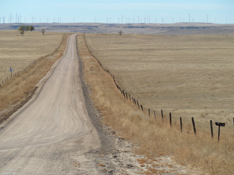 dirt gravel country secondary road leading to wind generators in the distance prairies barbed wire