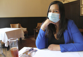 Latin adult woman with protection mask in restaurant with drink and food, new normal covid-19
