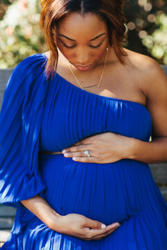 Pregnant woman sitting down on a park bench looking down at her belly