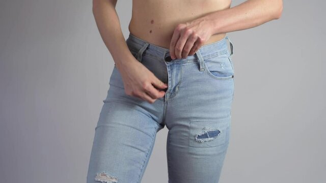 Woman is putting on a pair of jeans and buttoning zipper fastener then shows perfect waist after lost weight.