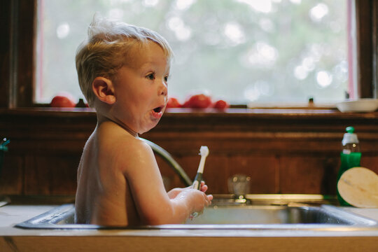 Happy And Suprised Child taking tub in kitchen sink