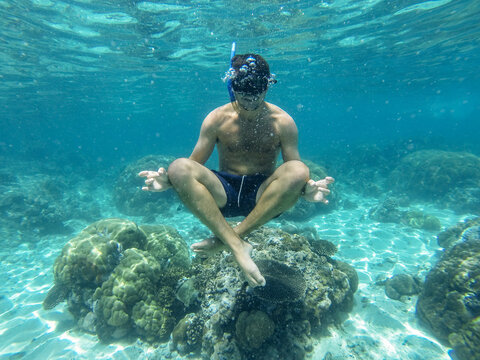 Young man snorkeling doing yoga position underwater