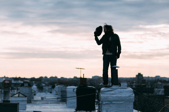 A scruffy man tips his hat on his Brooklyn rooftop