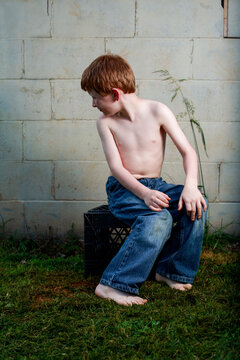 Young redheaded boy sitting on milk crate looking behind