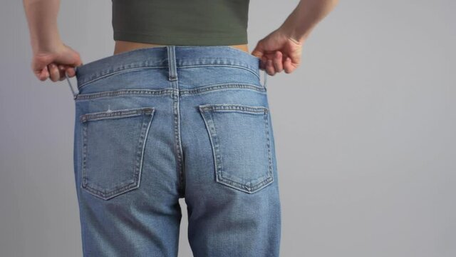 Slim woman in oversized jeans shows perfect waist after successful lost weight.