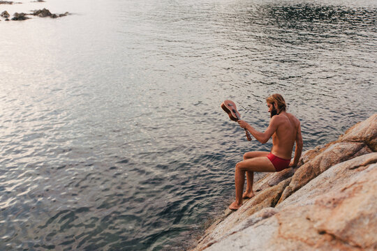 Young man on the rock above the sea with ukulele