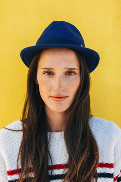 Portrait of a young beautiful woman wearing blue hat in front of yellow background.