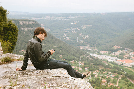 Young modern texting with mobile phone on the top of the mountain.