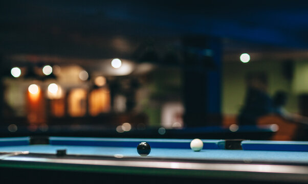 Pool billiard game in a nightclub with out of focus unrecognizable people playing in background