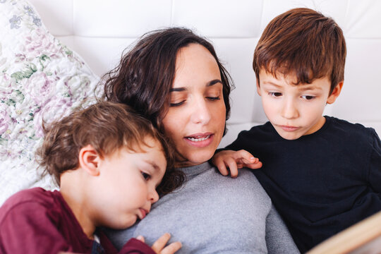 Young mother reading a book to her sons on a bed.