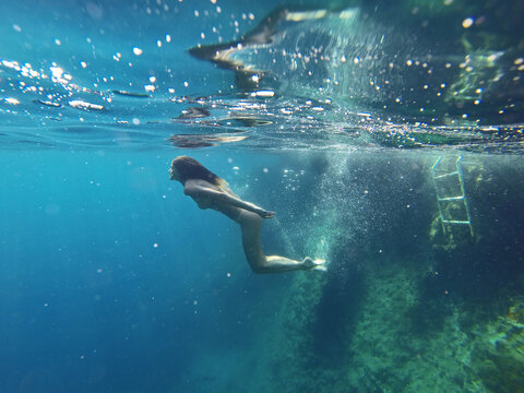 Skinny girl swimming underwater in clean blue sea