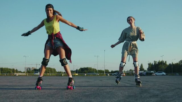 Smiling young pretty girls rolling skating outdoors having fun hold hands each other sport street legs friends rollerblading activity close up slow motion