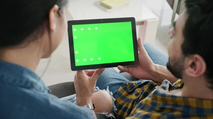 Young couple using tablet with green screen for internet and social media. Man and woman holding monitor with green monitor for website. Friends watching funny film on computer and laughing - Powered by Adobe