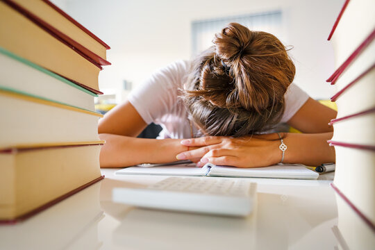 Front view on unknown Caucasian woman with head on her hands tired after study desperate between pile of books unable to solve the problem - education concept