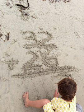 Young girl practices a math equation in the beach while on vacation