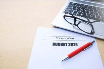 Text on budget 2021, pen, eyeglasses, and laptop on wooden table 