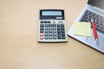 Blank notepad with pen on the laptop and a calculator on the wooden table 