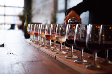Row of wine glasses being poured with multiple types of wine