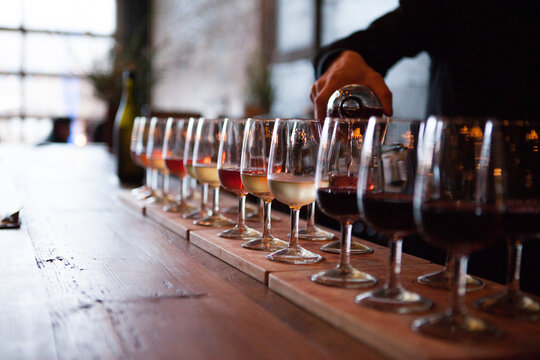 Row of wine glasses being poured with multiple types of wine