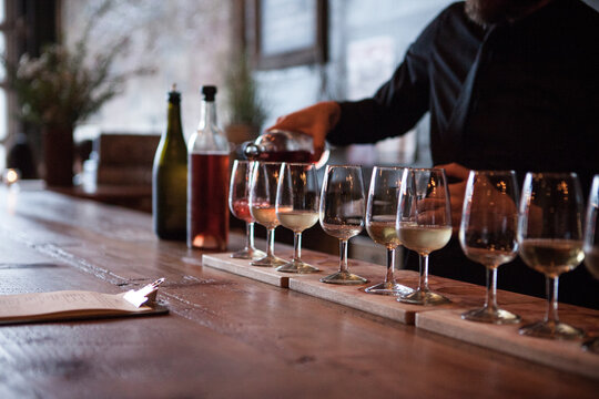 Row of wine glasses being poured with multiple types of wine