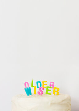 Message saying Older Wiser written on cake with colurful candles