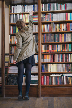 Girl stretching to grab a book from the bookshelf