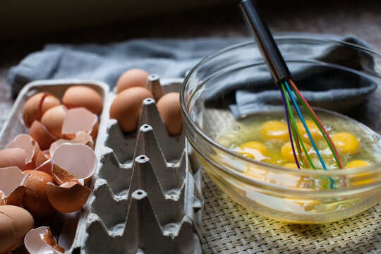 Many raw eggs in a bowl with the shells off to the side