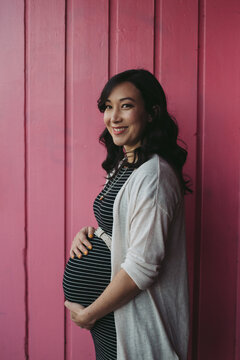 Pretty young pregnant woman standing near pink wall outside
