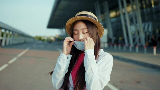 Nice-looking chinese woman removing coronavirus face mask smiling into camera. Beautiful cheerful girl rejoicing end of quarantine standing outdoor at sunlight.