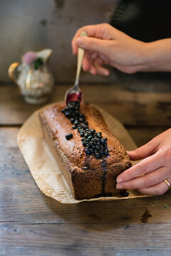 woman hand garnishing with blueberries sauce a homemade plumcake