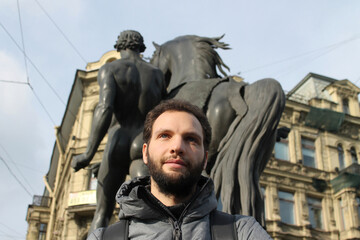 Smiling and looking away man standing on Anichkov bridge in Saint Petersburg with the horse statue on the background