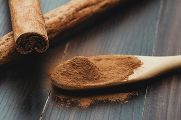 Cinnamon sticks and powder of cinnamon in a wooden spoon.