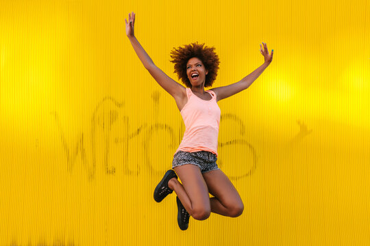 Happy Young Latin American Woman Jumping Against a Yellow Wall