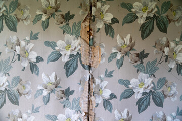 Peeling wallpaper on drywall plasterboard wall, with vintage white flowers and leaves