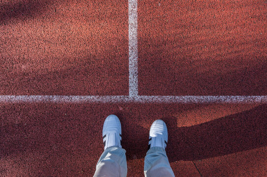 White sneakers outside red sport field, footsie, personal perspective